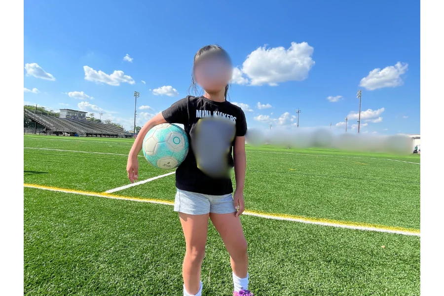 サッカー場の芝生でボールを抱えて立つ女の子