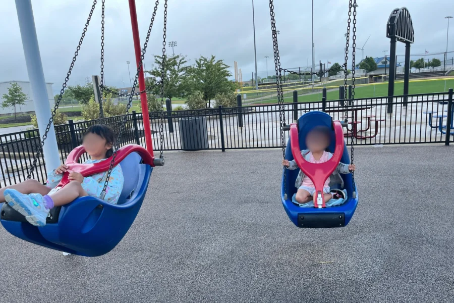 公園のブランコで、背もたれ付きの座面に座る2人の子供