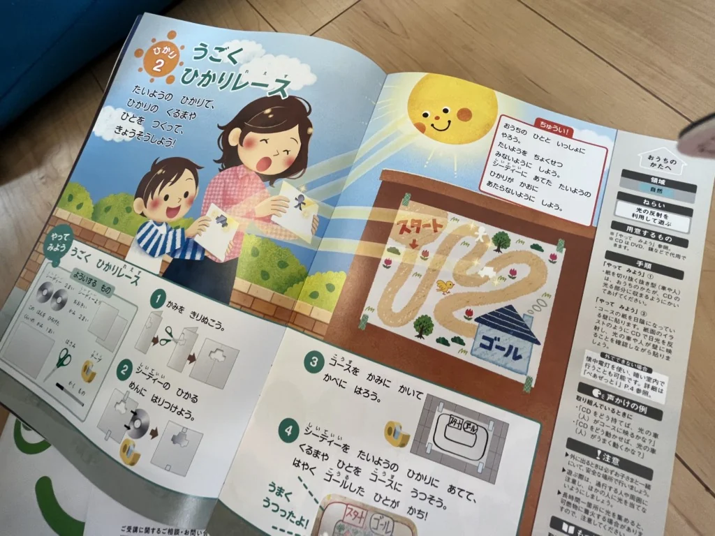 フローリングに広げた幼児ワークの見開き。太陽の光を使う「うごくひかりレース」の作り方と手順が図解されている
