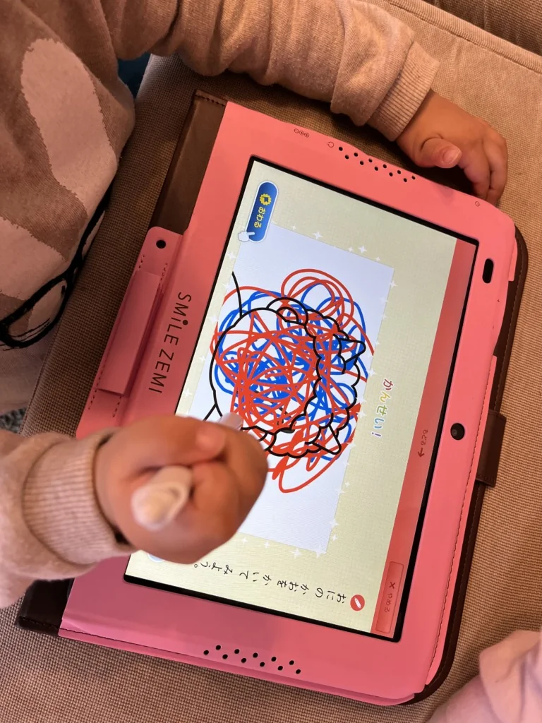 スマイルゼミのお絵かき画面に、赤・青・黒のペンでぐるぐると描かれた線。子供がペンを握りしめている